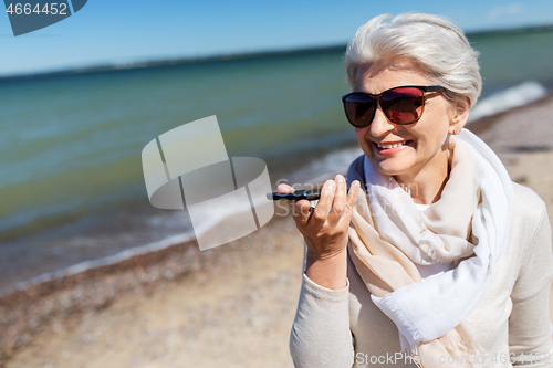 Image of old woman recording voice by smartphone on beach