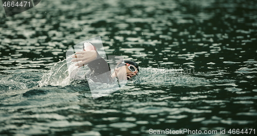 Image of triathlon athlete swimming on lake in sunrise wearing wetsuit