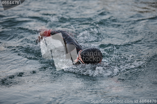 Image of triathlon athlete swimming on lake in sunrise wearing wetsuit