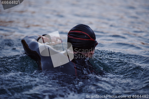 Image of triathlon athlete swimming on lake in sunrise wearing wetsuit