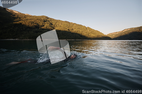 Image of triathlon athlete swimming on lake in sunrise wearing wetsuit