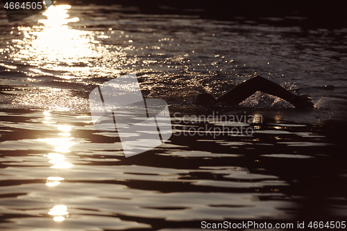 Image of triathlon athlete swimming on lake in sunrise wearing wetsuit