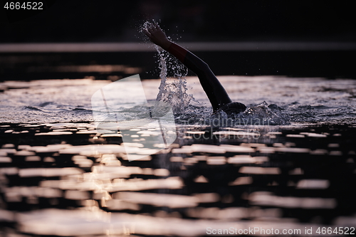 Image of triathlon athlete swimming on lake in sunrise wearing wetsuit