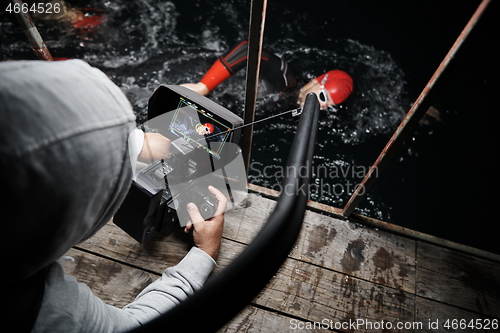 Image of videographer taking action shot of triathlon swimming athlete at night