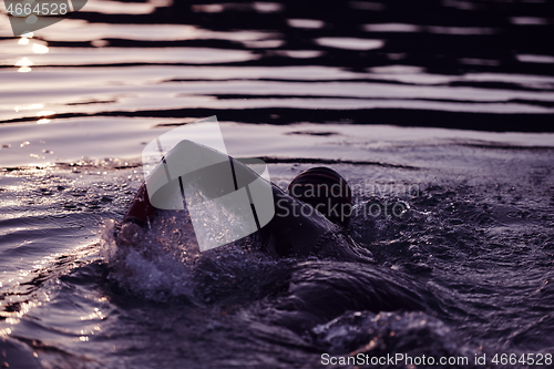 Image of triathlon athlete swimming on lake in sunrise wearing wetsuit