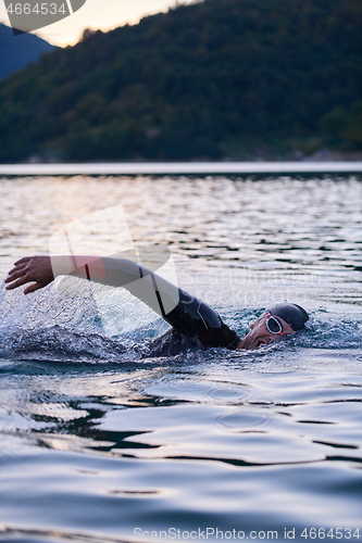 Image of triathlon athlete swimming on lake in sunrise wearing wetsuit