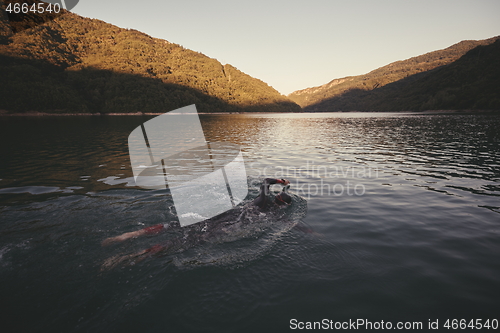 Image of triathlon athlete swimming on lake in sunrise wearing wetsuit