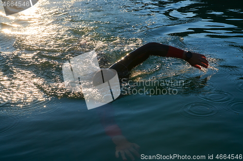 Image of triathlon athlete swimming on lake in sunrise wearing wetsuit