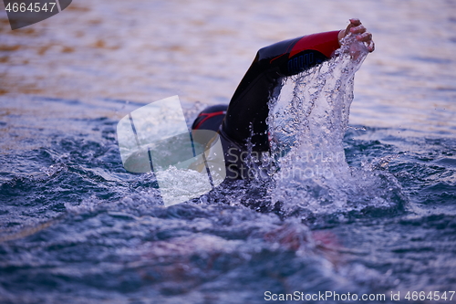 Image of triathlon athlete swimming on lake in sunrise wearing wetsuit