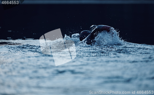 Image of triathlon athlete swimming on lake in sunrise wearing wetsuit