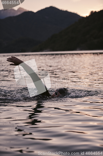 Image of triathlon athlete swimming on lake in sunrise wearing wetsuit