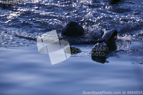 Image of triathlon athlete swimming on lake in sunrise wearing wetsuit