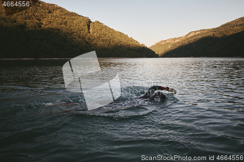 Image of triathlon athlete swimming on lake in sunrise wearing wetsuit