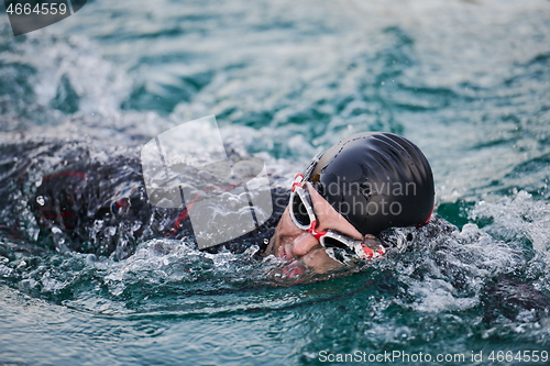 Image of triathlon athlete swimming on lake in sunrise wearing wetsuit