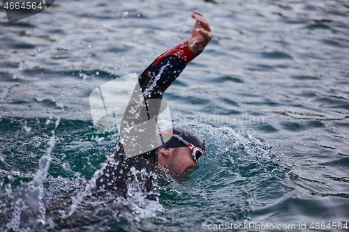 Image of triathlon athlete swimming on lake in sunrise wearing wetsuit