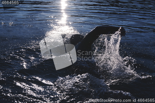 Image of triathlon athlete swimming on lake in sunrise wearing wetsuit