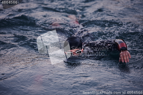 Image of triathlon athlete swimming on lake in sunrise wearing wetsuit