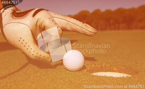 Image of man\'s hand putting golf ball in hole