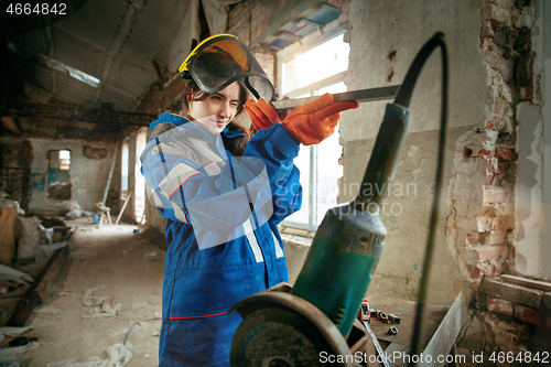 Image of Woman wearing helmet using male work tools