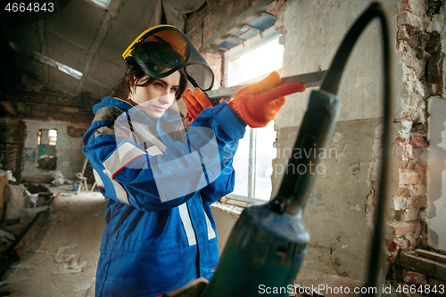 Image of Woman wearing helmet using male work tools