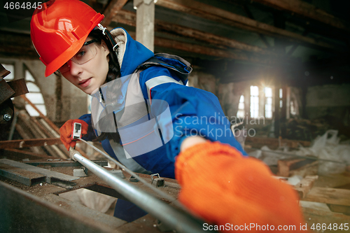 Image of Woman wearing helmet using male work tools