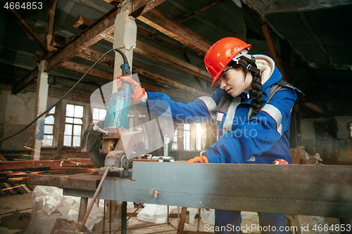 Image of Woman wearing helmet using male work tools