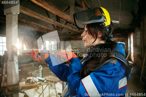 Image of Woman wearing helmet using male work tools