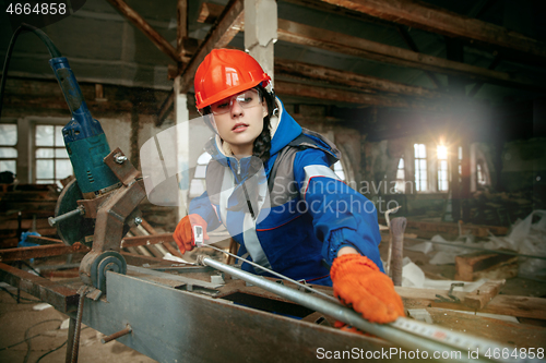 Image of Woman wearing helmet using male work tools