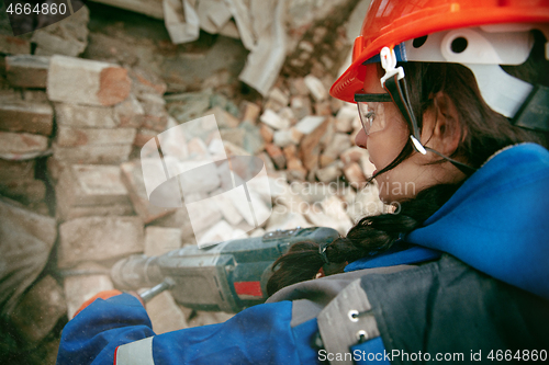 Image of Woman wearing helmet using male work tools