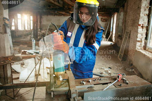 Image of Woman wearing helmet using male work tools