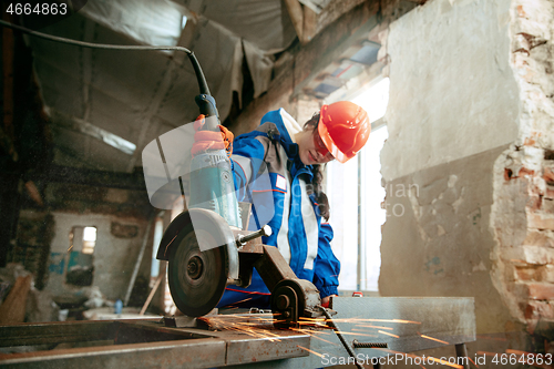 Image of Woman wearing helmet using male work tools