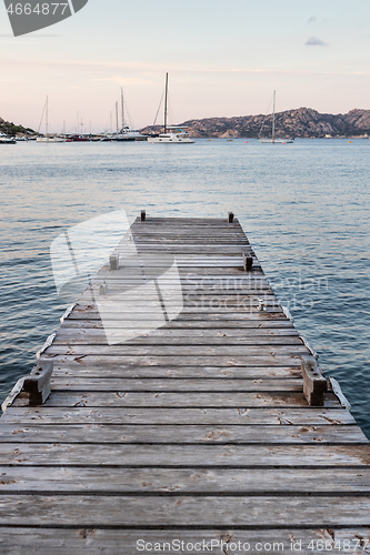 Image of Wooden pier and sailboats mooring in background at evening calm sea of marvellous Porto Rafael, Costa Smeralda, Sardinia, Italy. Symbol for relaxation, wealth, leisure activity