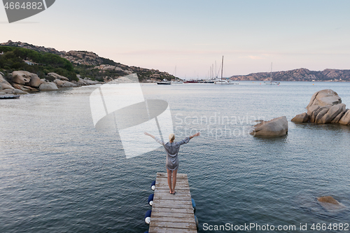 Image of Beautiful woman in luxury summer dress standing on wooden pier enjoying peaceful seascape at dusk. Vacation, resort and traveling.