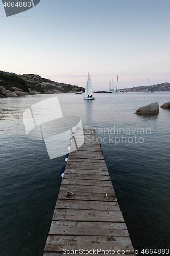 Image of Wooden pier and sailboats sailing in evening calm sea of marvellous Porto Rafael, Costa Smeralda, Sardinia, Italy. Symbol for relaxation, wealth, leisure activity