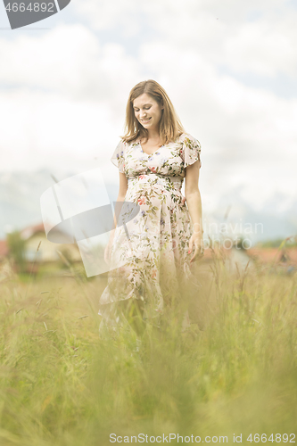 Image of Beautiful pregnant woman in white summer dress in meadow full of yellow blooming flowers.