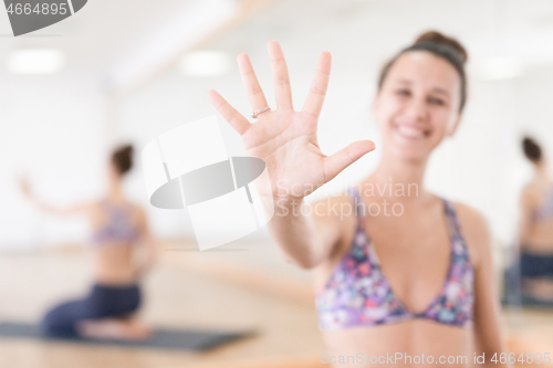 Image of Fit sporty active woman smiling, wearing fashion sportswear showing an open palm to the camera in yoga studio. Active urban lifestyle.