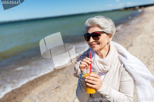 Image of senior woman drinking orange juice on beach