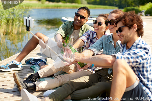 Image of friends with drinks taking selfie on lake pier