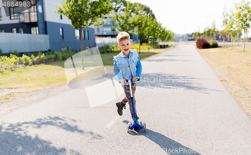 Image of happy little boy riding scooter in city