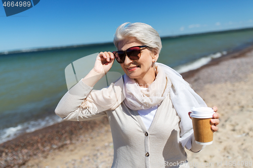 Image of senior woman drinking takeaway coffee on beach