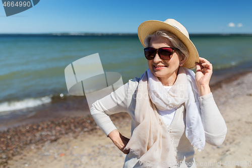 Image of happy senior woman in sunglasses and hat on beach