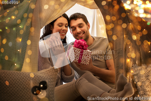 Image of happy couple with gift box in kids tent at home