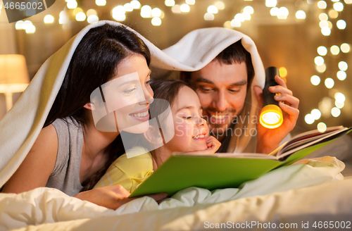 Image of happy family reading book in bed at night at home