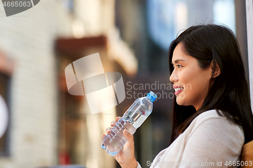 Image of woman drinking water sitting on wooden city bench