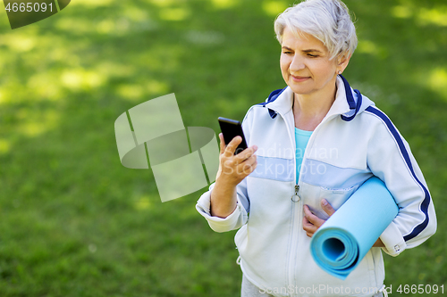 Image of old woman with exercise mat and smartphone at park