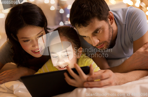 Image of family with tablet pc in bed at night at home