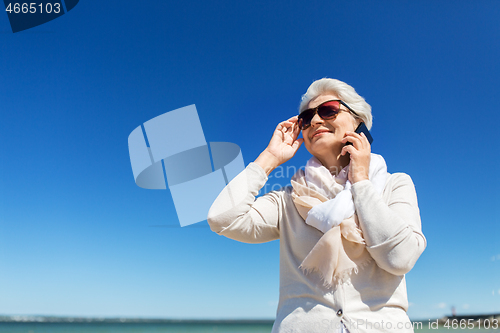 Image of senior woman calling on smartphone on beach