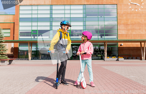 Image of happy school children in helmets riding scooters