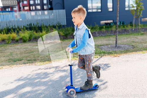 Image of happy little boy riding scooter in city