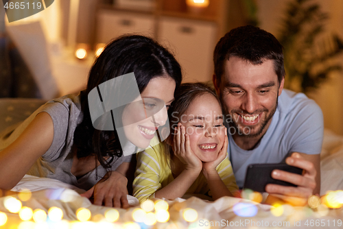 Image of happy family with smartphone in bed at night